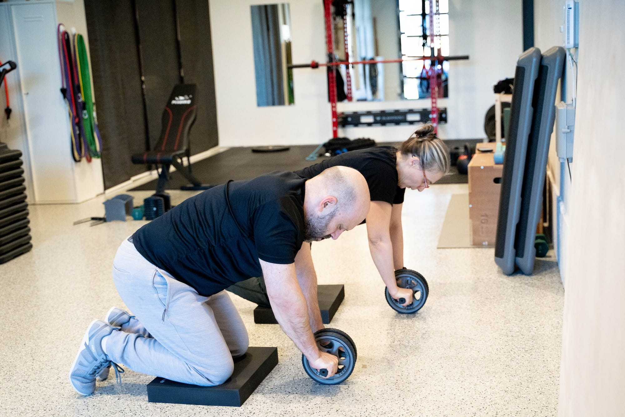 Two clients performing ab wheel rollouts on knee pads during a personal training session at Fit-InMotion At-Home Personal Training in Northeast Portland.