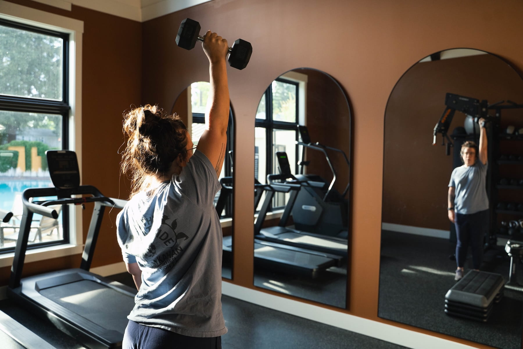 Client performing a single-arm dumbbell overhead press during an in-home personal training session in a Portland apartment gym.