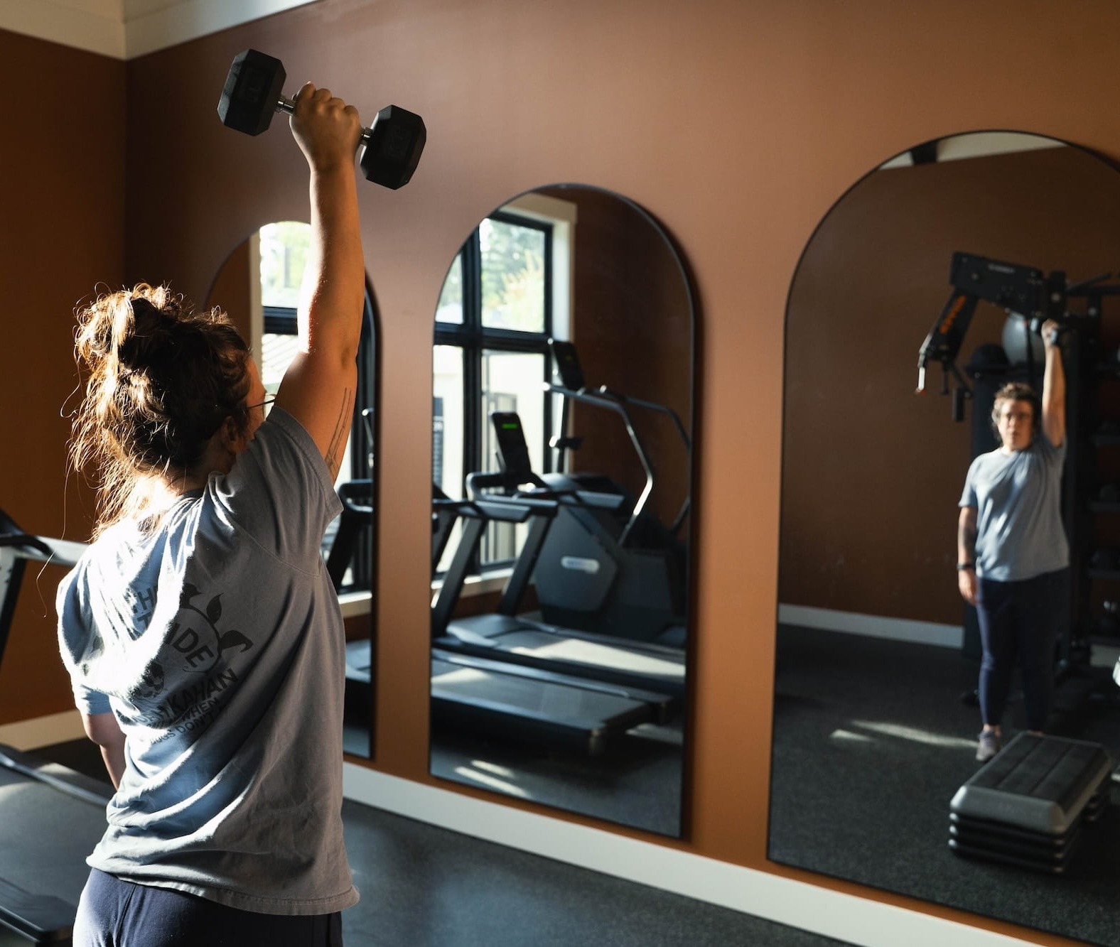 Client performing a single-arm dumbbell press during an in-home personal training session in a Portland apartment gym.