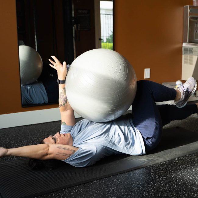Woman performing a dead bug exercise with a stability ball to strengthen her core and improve trunk stability.